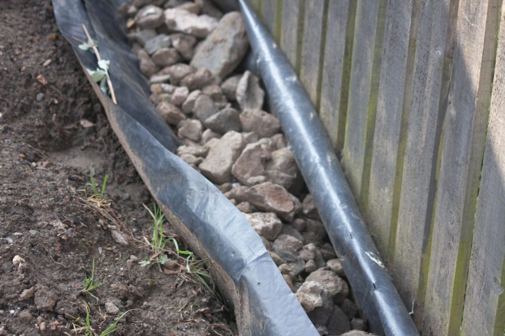 fence, and in front a ditch lined with black plastic and filled with stones