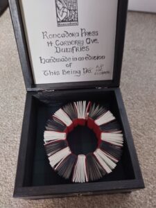 bracelet of tiny linked books with alternating black and white edged pages and red covers in a black box