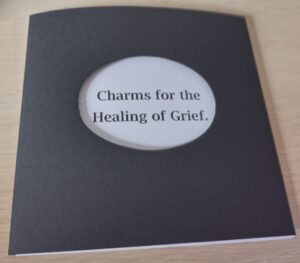 cover of book. Black paper with a white oval cutout the title Charms for the Healing of Grief in black type