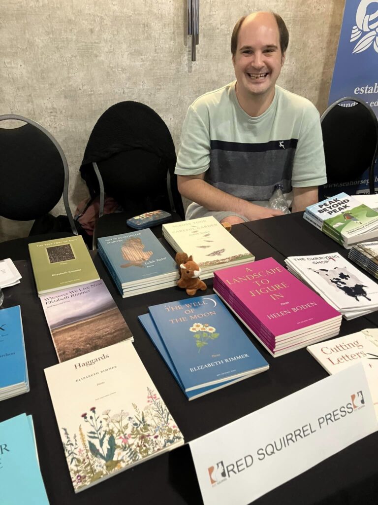 Squirrel poet Edwin Stockdale minding the sales desk at the Red Squirrel Press showcase. Books by Judith Taylor, Helen Boden, Hazel Cameron Elizzabeth Rimmer and Edwin Stockdale on the table.
